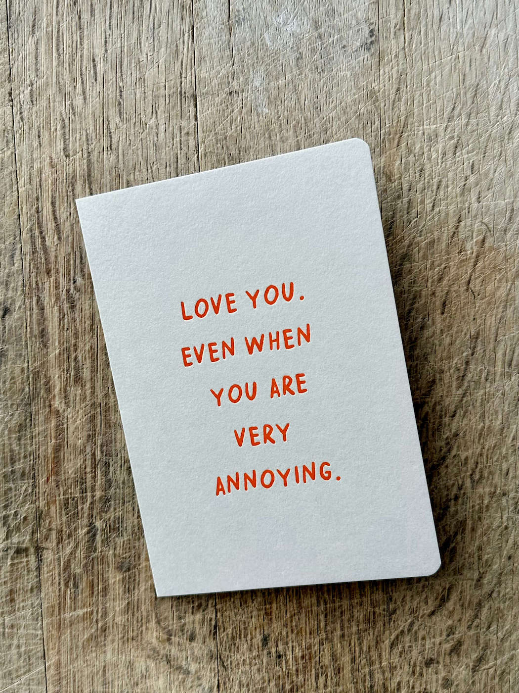 Notebook with text 'Love you even when you are very annoying' on a wooden surface