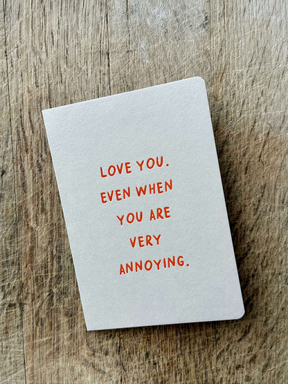 Notebook with text 'Love you even when you are very annoying' on a wooden surface